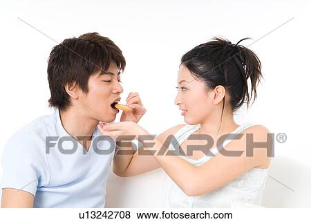 Stock Photo - Young woman feeding her boyfriend cookie. Fotosearch