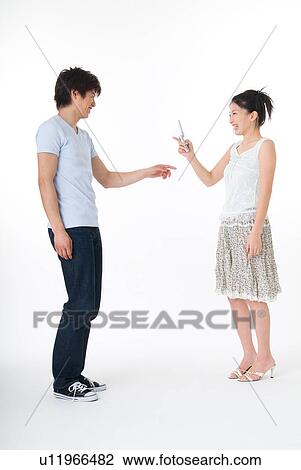 Stock Image - Young woman photographing her boyfriend with cameraphone. Fotosearch