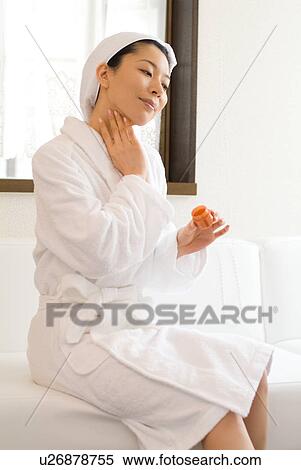 Stock Photography - A mid adult woman in bathrobe applying moisturizer. Fotosearch