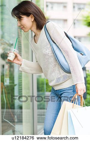 Stock Photograph - A mid adult woman looking into shop window. Fotosearch