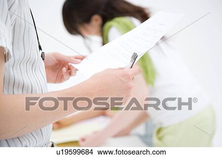 Picture - A young man looking at document with a woman in background. Fotosearch