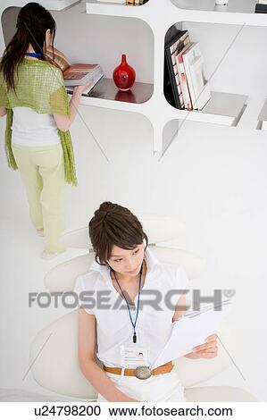 A young woman reading document with a young woman standing behind View Large Photo Image Stock Image - A young woman reading document with a young woman standing behind. Fotosearch