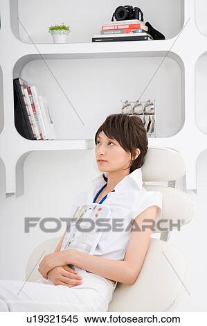 Stock Photography - A young woman sitting on sofa holding books. Fotosearch