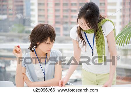 Two young women looking at document View Large Photo Image Stock Photograph - Two young women looking at document. Fotosearch