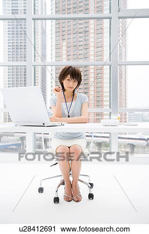 Young woman sitting at her desk View Large Photo Image Stock Image - Young woman sitting at her desk. Fotosearch