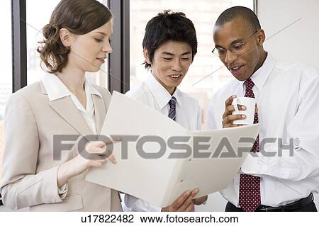 Stock Image - Three business people looking at file. Fotosearch