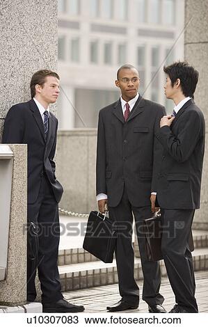 Stock Image - Three businessmen talking in front of building. Fotosearch