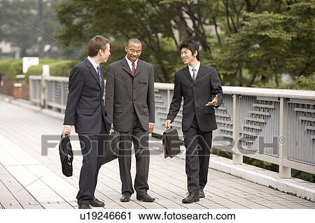 Three businessmen talking while walking View Large Photo Image Stock Image - Three businessmen talking while walking. Fotosearch