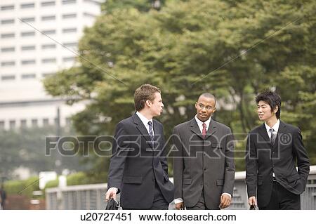 Stock Image - Three businessmen talking while walking. Fotosearch
