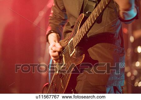 Stock Photo - Young man playing electric guitar on stage. Fotosearch