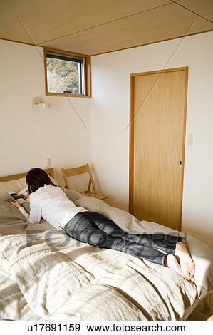 Stock Photo - Young woman reading book on bed. Fotosearch