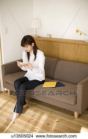 Picture - Young woman reading book sitting on sofa. Fotosearch