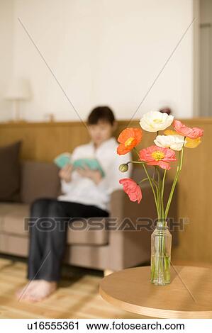 Stock Image - Young woman reading book sitting on sofa. Fotosearch