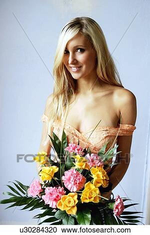 Stock Image - Young woman in see-through top holding bouquet of flowers, smiling. Fotosearch