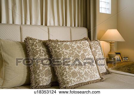 Picture - Detail of neutral toned decorative pillows on bed with lamp.. Fotosearch