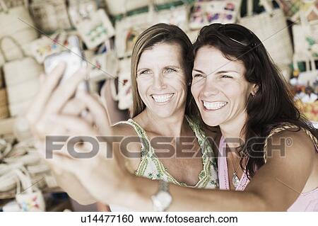 Stock Image - Close-up of two mid adult women holding a mobile phone and smiling. Fotosearch