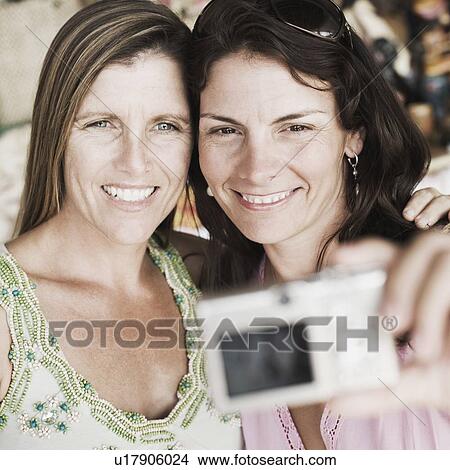 Close-up of two mid adult women taking a photograph of themselves View Large Photo Image Picture - Close-up of two mid adult women taking a photograph of themselves. Fotosearch