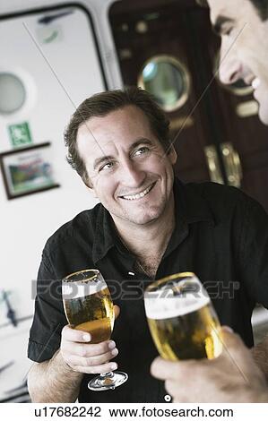 Mid adult man and his friend holding beer glasses and smiling View Large Photo Image Stock Image - Mid adult man and his friend holding beer glasses and smiling. Fotosearch