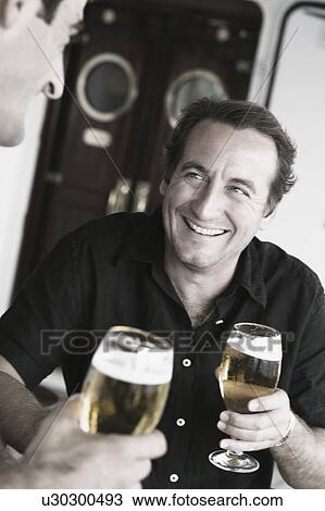 Mid adult man and his friend holding beer glasses and smiling View Large Photo Image Stock Image - Mid adult man and his friend holding beer glasses and smiling. Fotosearch