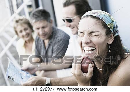 Mid adult woman holding an apple with her friends sitting beside her View Large Photo Image Stock Photo - Mid adult woman holding an apple with her friends sitting beside her. Fotosearch