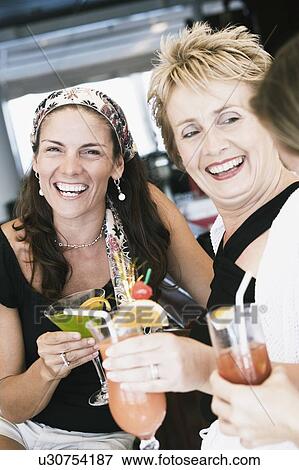 Stock Photo - Portrait of a mid adult woman and a mature woman holding glasses of cocktail and smiling. Fotosearch