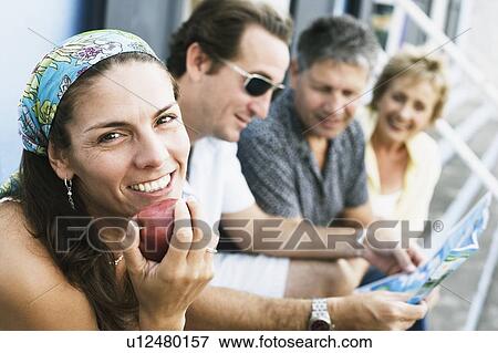 Portrait of a mid adult woman eating an apple with her friends sitting beside her View Large Photo Image Stock Photo - Portrait of a mid adult woman eating an apple with her friends sitting beside her. Fotosearch
