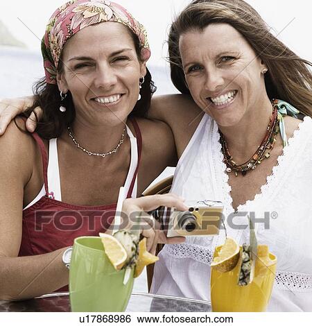 Portrait of two mid adult women holding a digital camera and smiling View Large Photo Image Stock Photograph - Portrait of two mid adult women holding a digital camera and smiling. Fotosearch