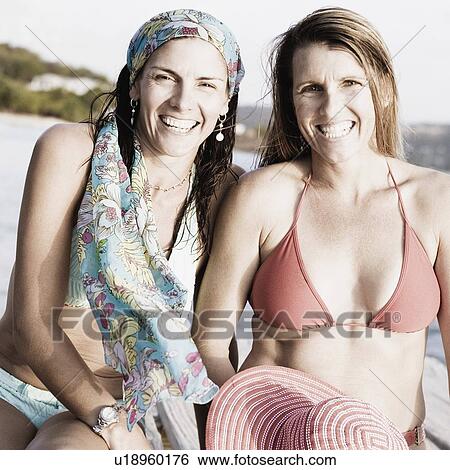 Stock Photograph - Portrait of two mid adult women sitting on a pier and smiling. Fotosearch