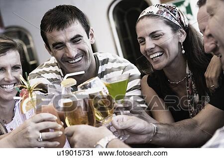 Stock Image - Three mid adult men and two mid adult women toasting their drinks. Fotosearch