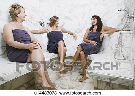 Stock Photo - Two mid adult women and a mature woman sitting in the bathroom and smiling. Fotosearch