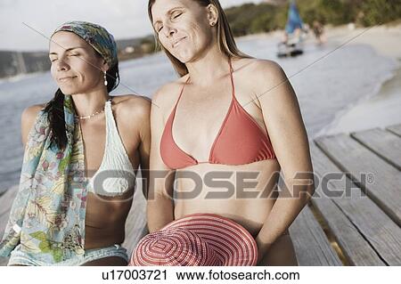 Two mid adult women sitting on a pier View Large Photo Image Stock Image - Two mid adult women sitting on a pier. Fotosearch