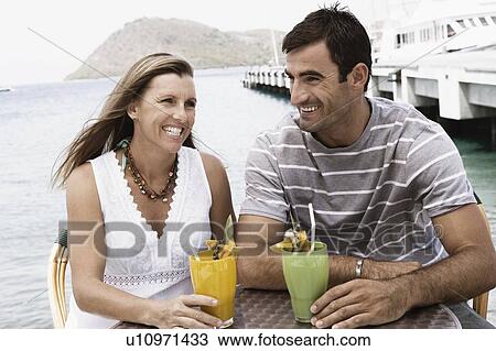 Close-up of a mid adult couple holding glasses of juice and smiling View Large Photo Image Stock Image - Close-up of a mid adult couple holding glasses of juice and smiling. Fotosearch