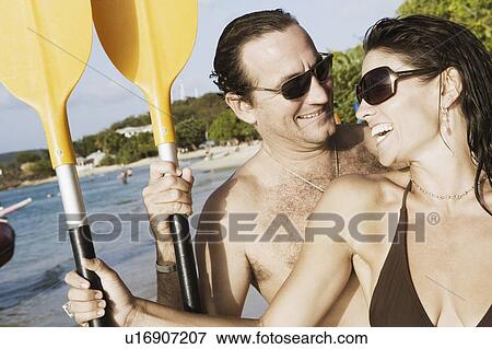 Stock Photo - Close-up of a mid adult couple holding oars on the beach. Fotosearch