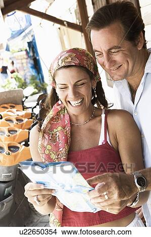 Picture - Close-up of a mid adult couple looking at a catalog and smiling. Fotosearch