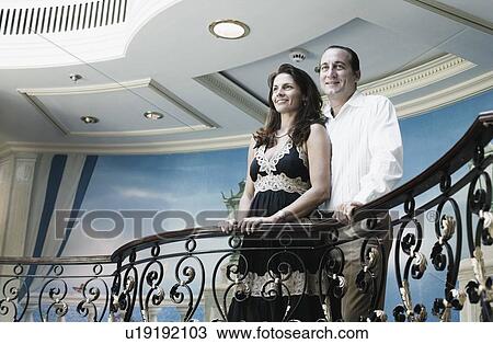 Stock Image - Low angle view of a mid adult couple standing at the balcony of a ship and smiling. Fotosearch