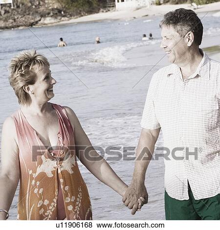 Mature woman holding a senior man's hand and walking on the beach View Large Photo Image Stock Photo - Mature woman holding a senior man's hand and walking on the beach. Fotosearch