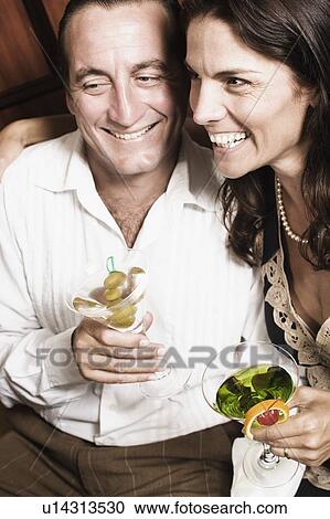 Mid adult couple holding glasses of cocktail and smiling View Large Photo Image Stock Image - Mid adult couple holding glasses of cocktail and smiling. Fotosearch