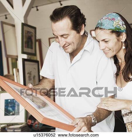 Stock Image - Mid adult couple purchasing paintings from a store. Fotosearch