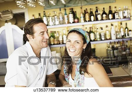 Mid adult couple sitting at a bar counter and smiling View Large Photo Image Stock Photo - Mid adult couple sitting at a bar counter and smiling. Fotosearch
