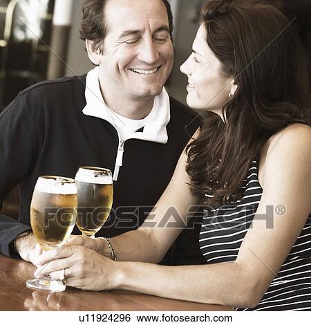 Mid adult couple sitting in a bar and holding beer in stem glasses View Large Photo Image Stock Photograph - Mid adult couple sitting in a bar and holding beer in stem glasses. Fotosearch