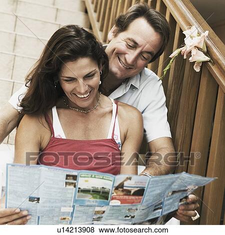 Mid adult couple sitting on a staircase and looking at a brochure and smiling View Large Photo Image Stock Photo - Mid adult couple sitting on a staircase and looking at a brochure and smiling. Fotosearch