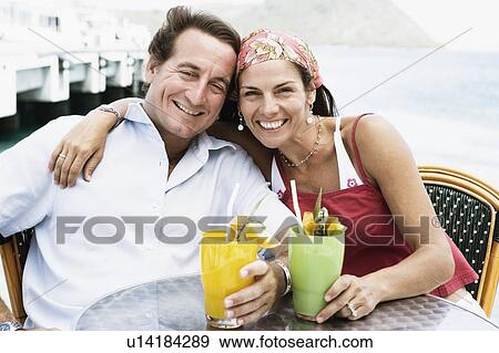 Portrait of a mid adult couple holding glasses of juice and smiling View Large Photo Image Stock Photo - Portrait of a mid adult couple holding glasses of juice and smiling. Fotosearch