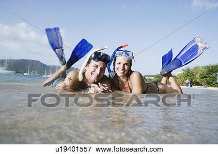 Stock Photo - Portrait of a mid adult couple lying on the beach and smiling. Fotosearch