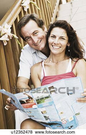 Portrait of a mid adult couple sitting on a staircase and holding a brochure View Large Photo Image Stock Photo - Portrait of a mid adult couple sitting on a staircase and holding a brochure. Fotosearch