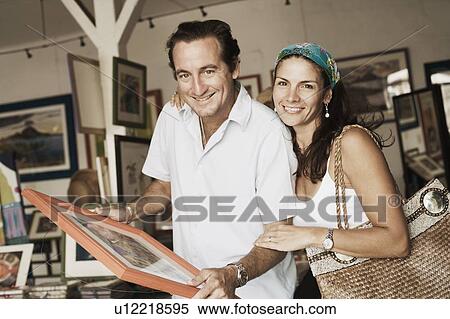 Stock Photography - Portrait of a mid adult couple purchasing paintings from a store. Fotosearch