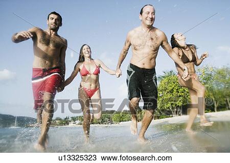 Stock Image - Two mid adult couples running on the beach. Fotosearch