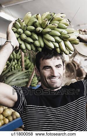 Stock Photo - Close-up of a mid adult man carrying a bunch of bananas on his head. Fotosearch