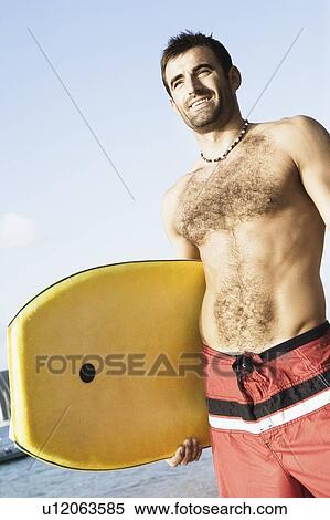 Low angle view of a mid adult man holding a surfboard View Large Photo Image Stock Photography - Low angle view of a mid adult man holding a surfboard. Fotosearch