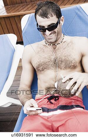 Mid adult man reclining on a lounge chair and listening to music on an MP3 player View Large Photo Image Stock Image - Mid adult man reclining on a lounge chair and listening to music on an MP3 player. Fotosearch