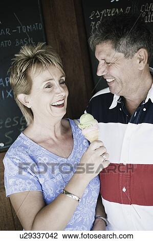 Stock Image - Mature woman holding an ice-cream cone with a senior man smiling beside her. Fotosearch